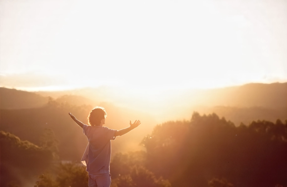Man met open armen groet de zon in de bergen